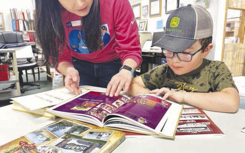 Volunteer Kaleigh Biegler helps first grader Ryker Bridges find some people he knows in the history yearbooks.