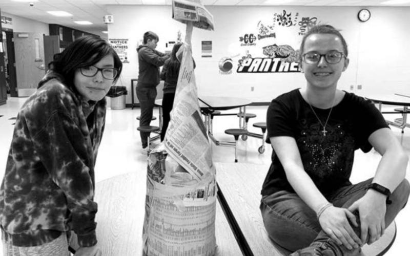 Eighth graders McKayla Fool Bear and Maria Scherer with the tower they constructed from newspapers.