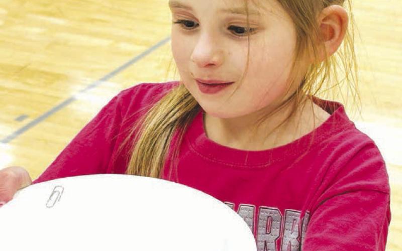 Thea Eigelaar learns how a magnet held under a paper plate moves a paper clip on top of the plate.