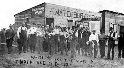 Before Timber Lake had a post office, mail was distributed at the First State Bank and Waterbury Hardware. A young Wenzel Leff is pictured (left of center), reading a letter.