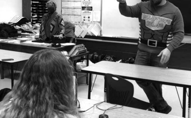 Teacher Ryan Gimbel, wearing his holiday sweater, addresses one of his high school classes.