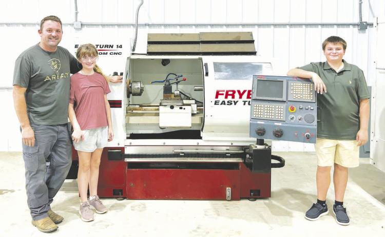 Heinrich Muller (left) with his children, Cecilia (middle) and Conrad (right) with some of the machinery in the new KOTA shop.