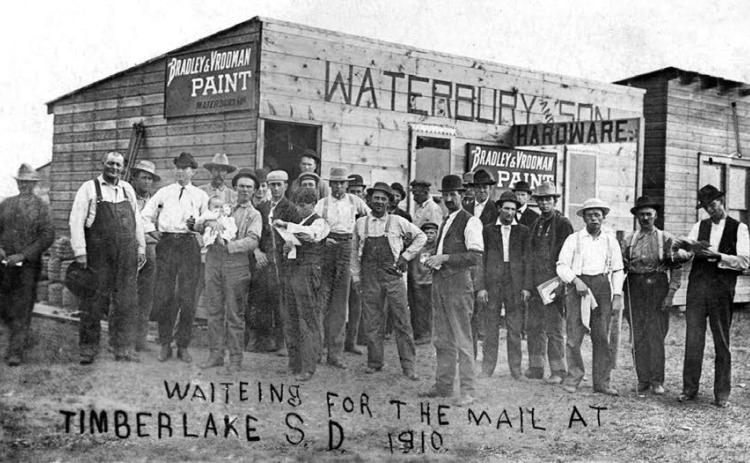 Before Timber Lake had a post office, mail was distributed at the First State Bank and Waterbury Hardware. A young Wenzel Leff is pictured (left of center), reading a letter.